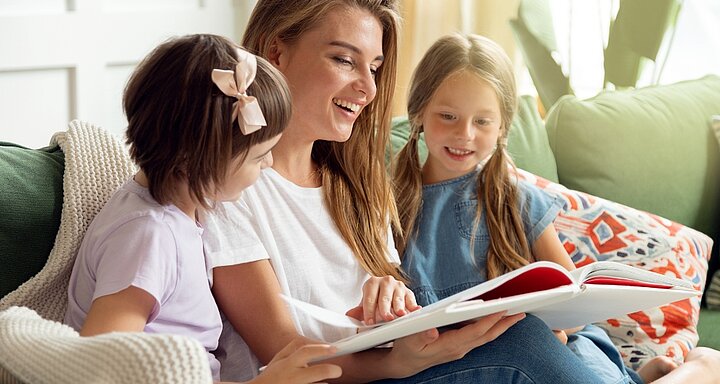 Dospělý čte dětem z knihy jako podpora rozvoje řeči ve školce.