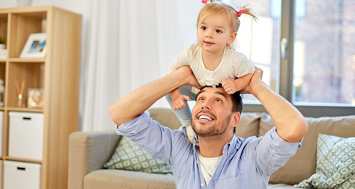 Dospělý si hraje s batoletem na ramenou.