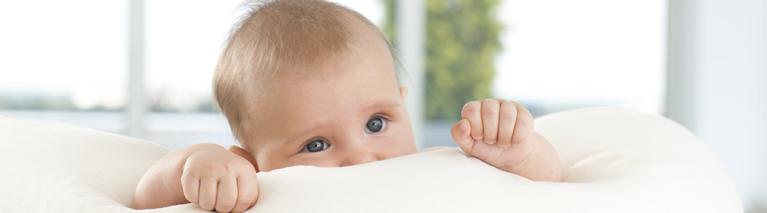 Přes bílou deku vykukuje dítě s modrýma očima.