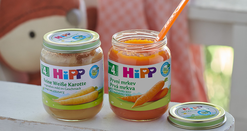 Na bílé ploše jsou umístěny dvě skleněné nádoby s oranžovým a hnědým obsahem, označené nápisem "HIPP".