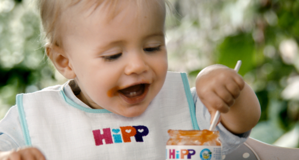 Dítě s bryndáčkem s nápisem "HIpp" jí ze sklenice.
