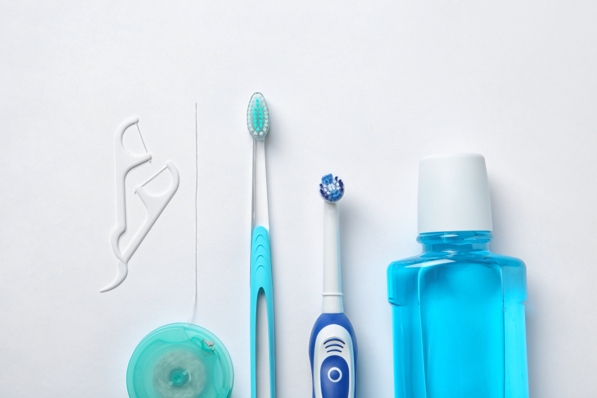 Sbírka předmětů pro zubní hygienu včetně manuálního zubního kartáčku, elektrického zubního kartáčku, zubní nitě a lahvičky ústní vody.