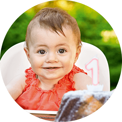 A baby in a high chair with a number 1 candle on a cake.