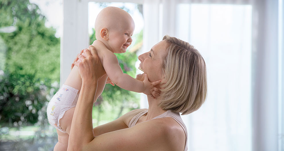 A woman lifts a baby in a room with a window.