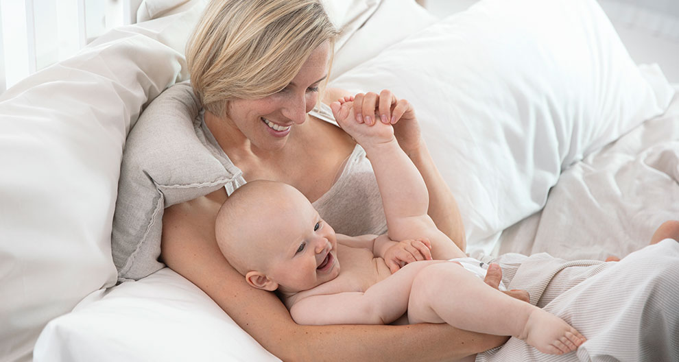 A woman reclines on a bed, holding a laughing baby.