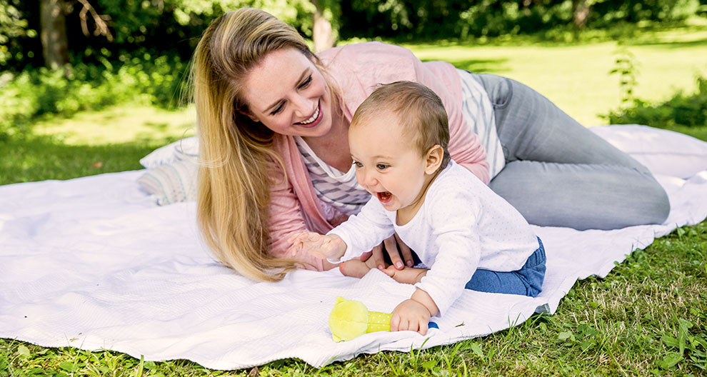 A woman and a baby are lying on a blanket in a grassy area.