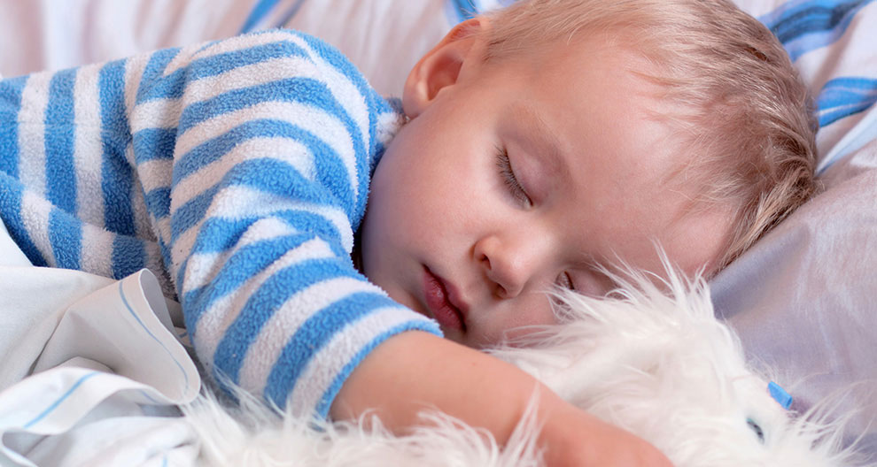 A child is sleeping, wearing a blue and white striped shirt, with a white fluffy toy beside them.