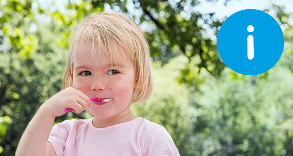 A young child brushes their teeth outdoors.